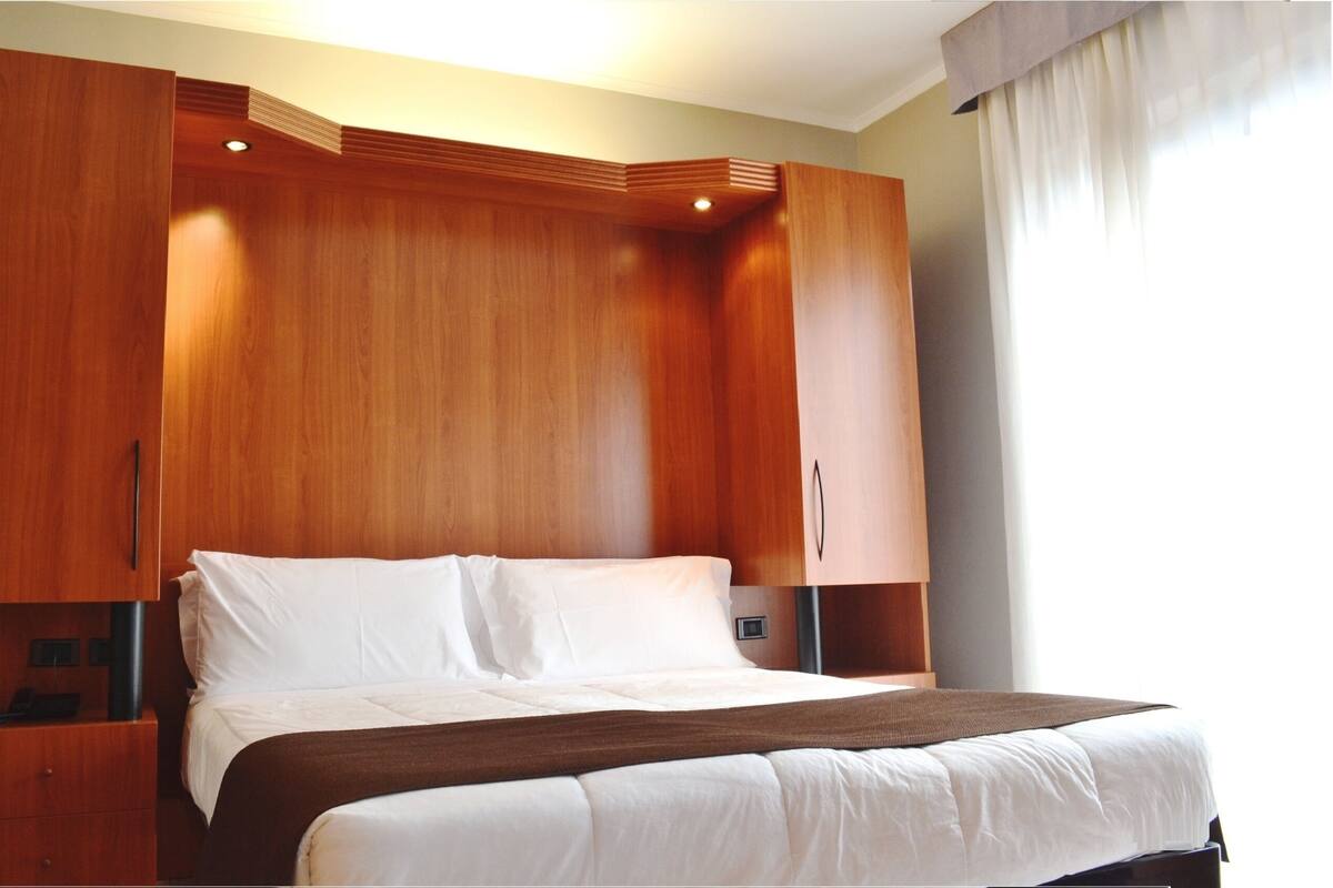 Een hotelkamer met een groot bed, een houten garderobe en een nachtkastje.