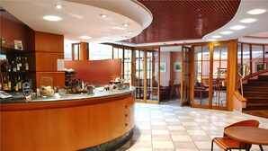 Een moderne bar met een gebogen toonbank, houten lambrisering en uitzicht door glazen deuren op een zithoek met een trap.