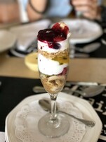 A dessert in a glass on a white plate with a lace doily underneath.