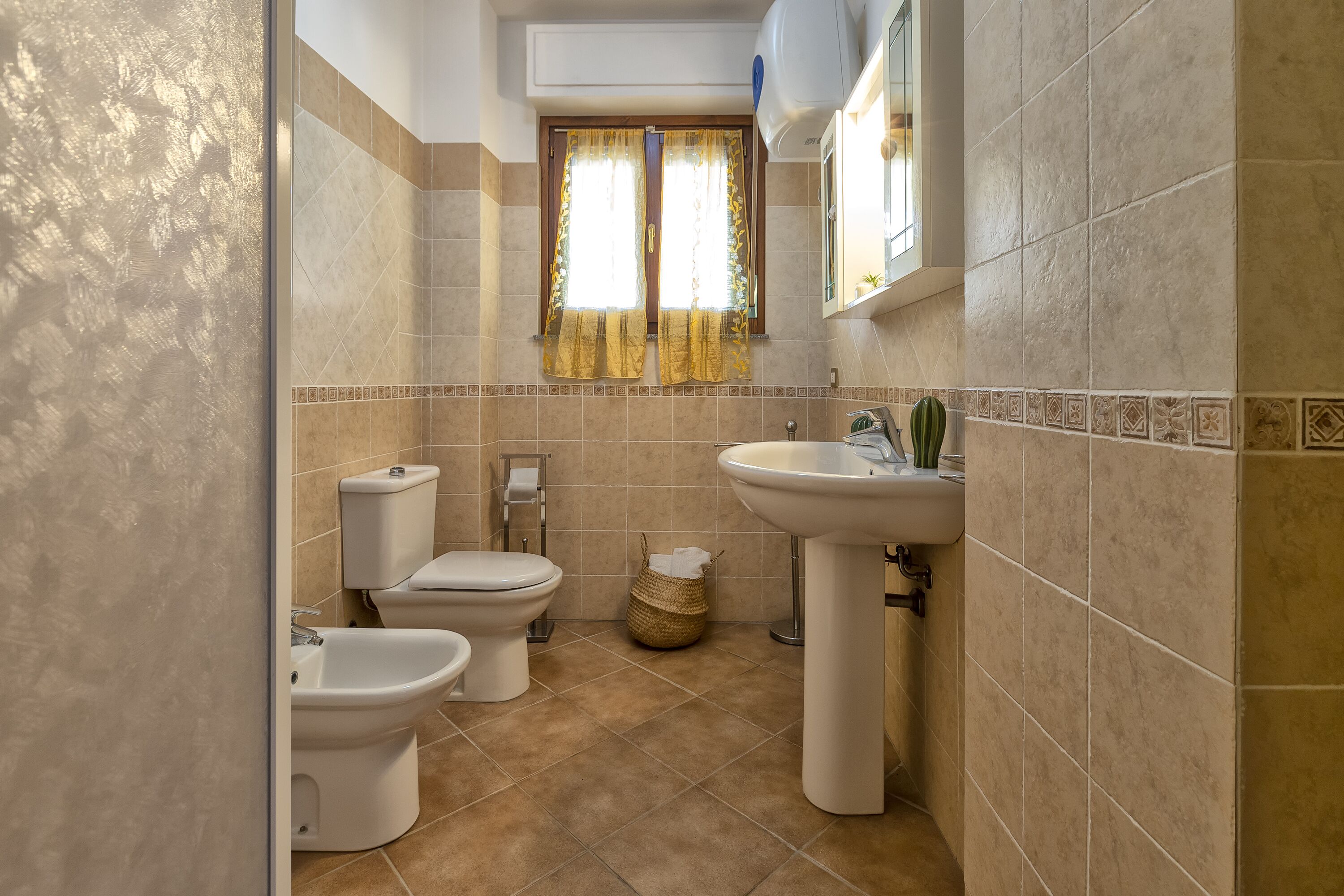 Een badkamer met twee toiletten, een bidet, een wastafel en een raam met gordijnen.