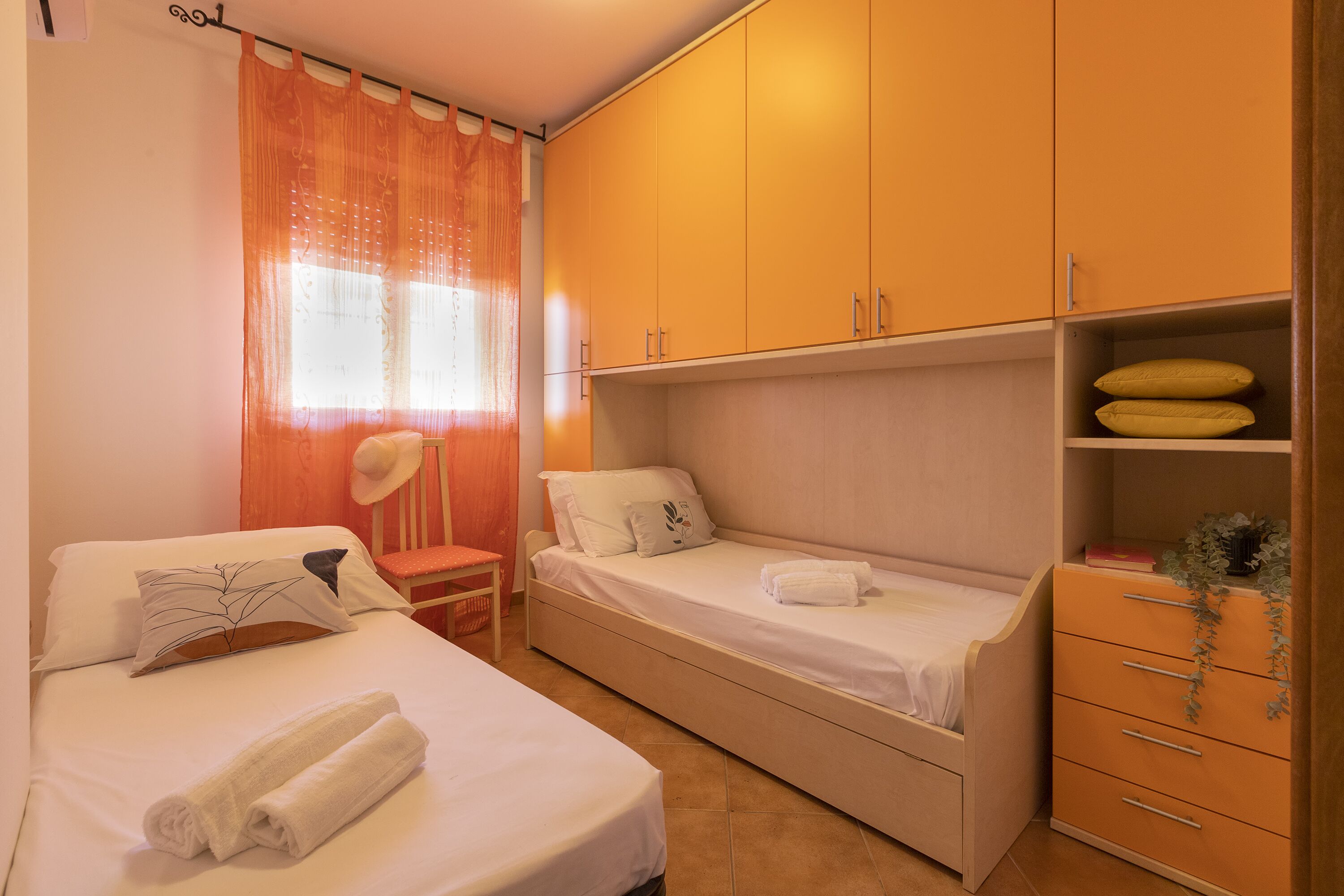 A bedroom with two single beds, a wooden wardrobe, and a small desk.