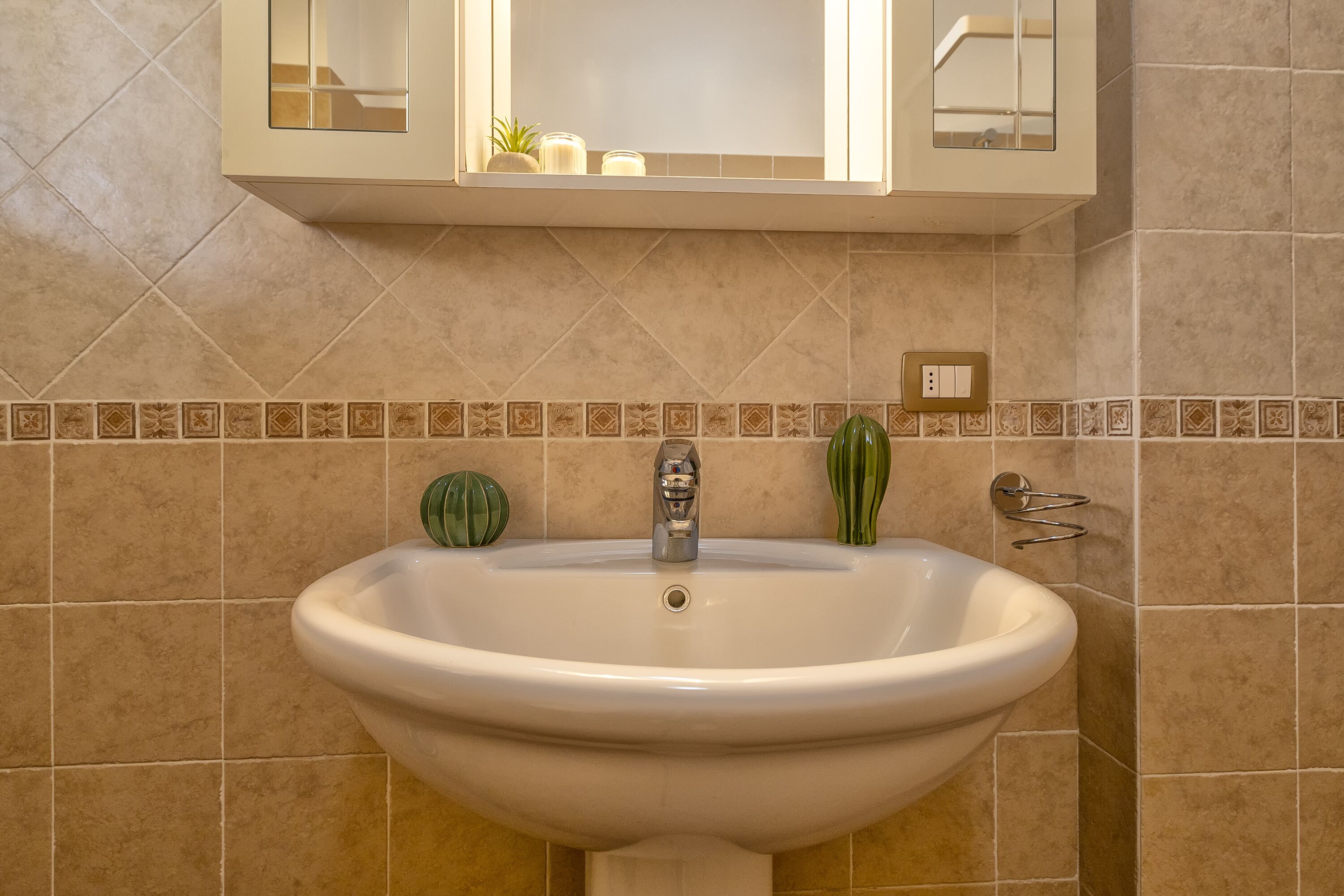 Une salle de bain avec un lavabo blanc, un miroir au-dessus et un mur recouvert de carreaux derrière le lavabo.
