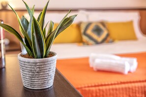A potted plant on a wooden table in a hotel room with a bed and a yellow pillow in the background.