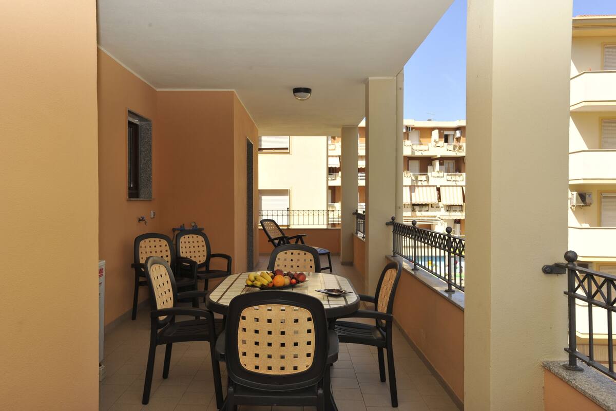 A balcony with a table set for dining, surrounded by chairs, and a view of adjacent buildings.