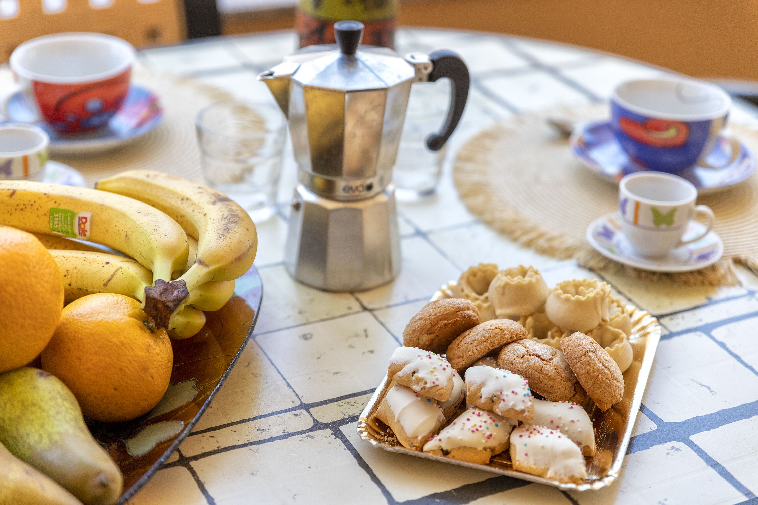 A table with a coffee pot, a plate of cookies, and a bowl of fruit.
