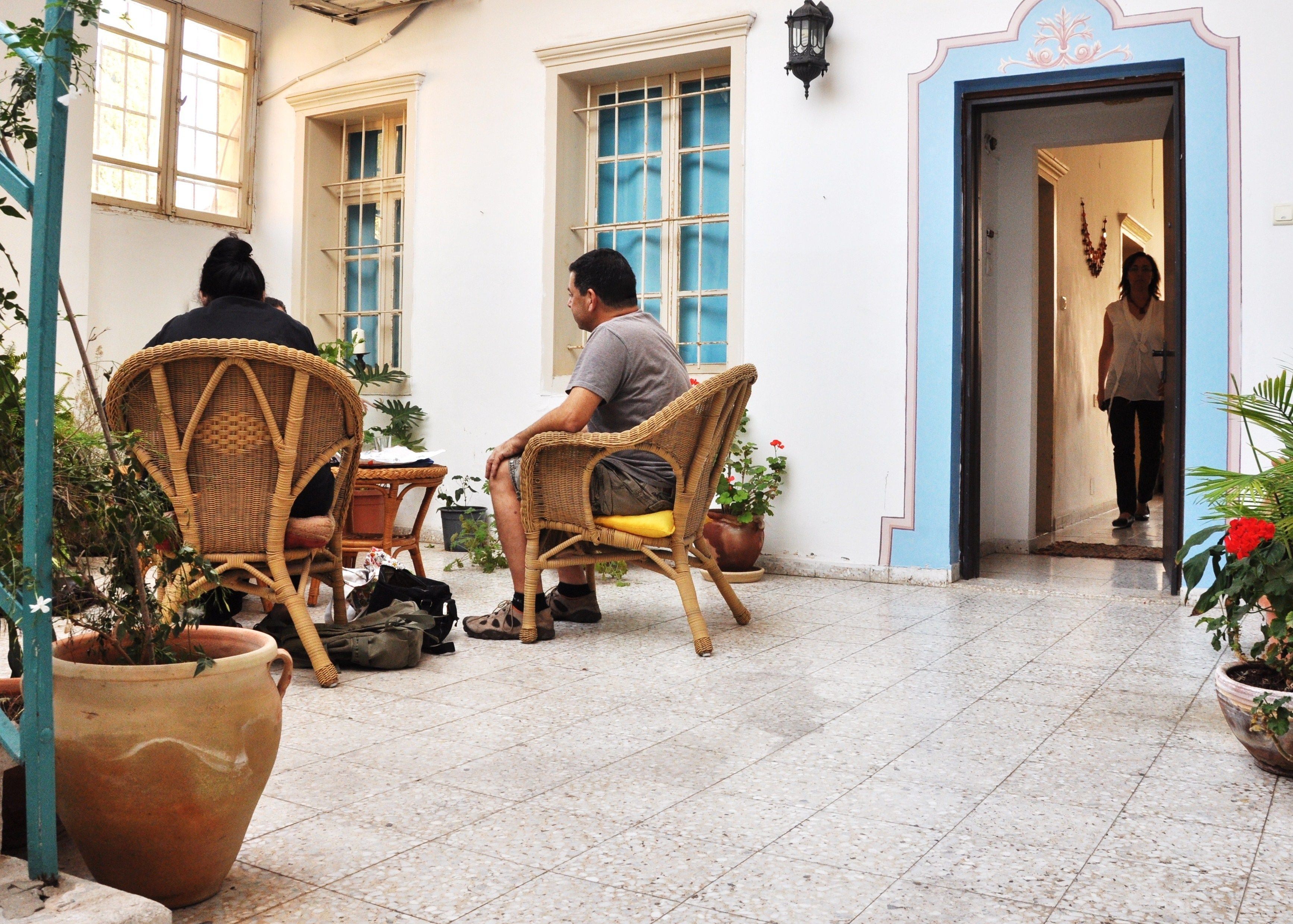 A courtyard with wicker chairs, potted plants, and a tiled floor.