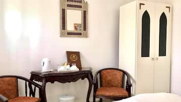 Una habitación con una cama, dos sillas, una mesa con una tetera, un espejo decorativo y un armario de dos puertas.