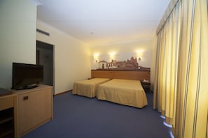 Habitación de hotel con dos camas individuales, un televisor sobre un mueble y un mural de un castillo en la pared.