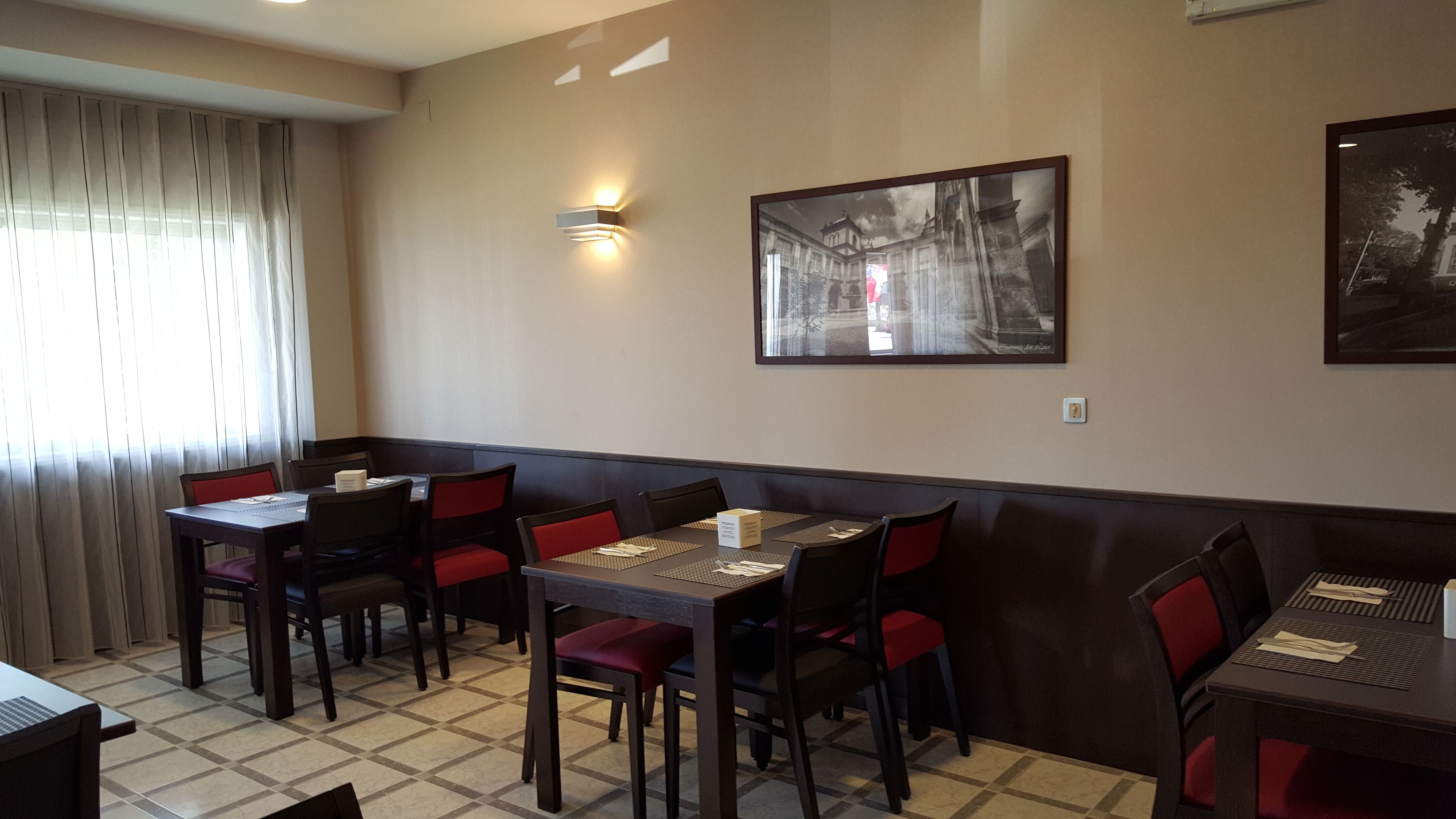 A restaurant with booths and tables, a large framed picture on the wall, and a window with curtains.
