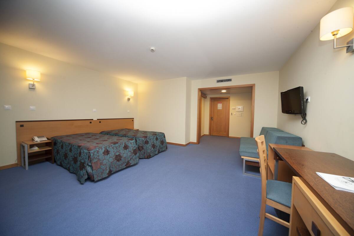 A hotel room with two beds, a desk, a chair, a television, and a door leading to another room.