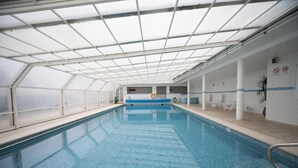 An indoor swimming pool with a glass ceiling, white walls, and a blue pool edge. - Hotel Feira Pedra Bela (Santa Maria da Feira)