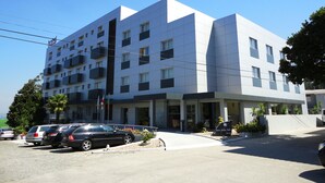 A modern hotel with a white facade, multiple balconies, and a parking area with several cars. - Hotel Feira Pedra Bela (Santa Maria da Feira)