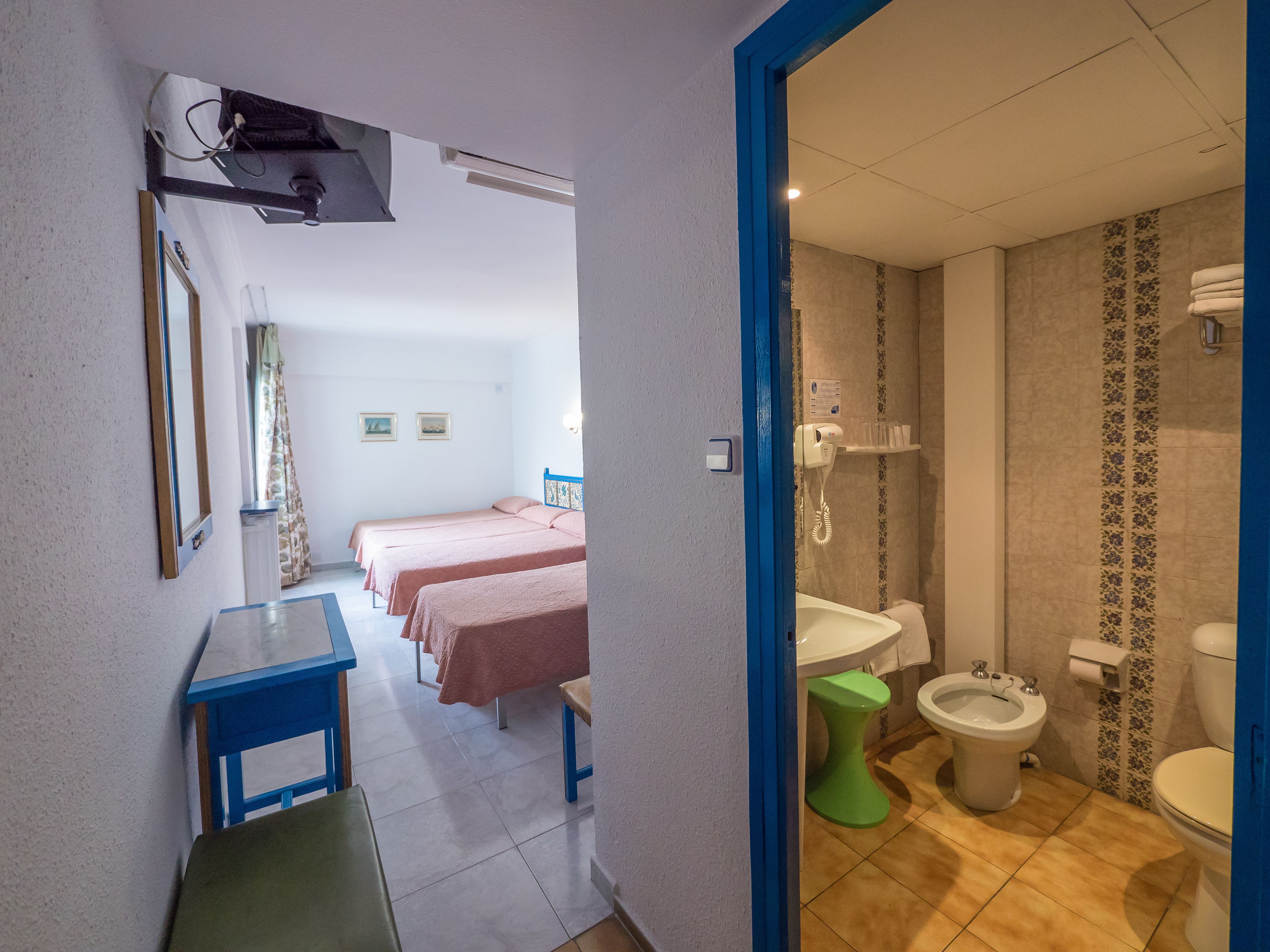 Habitación de hotel con dos camas individuales, un escritorio, una silla y baño con inodoro, bidé y lavamanos.