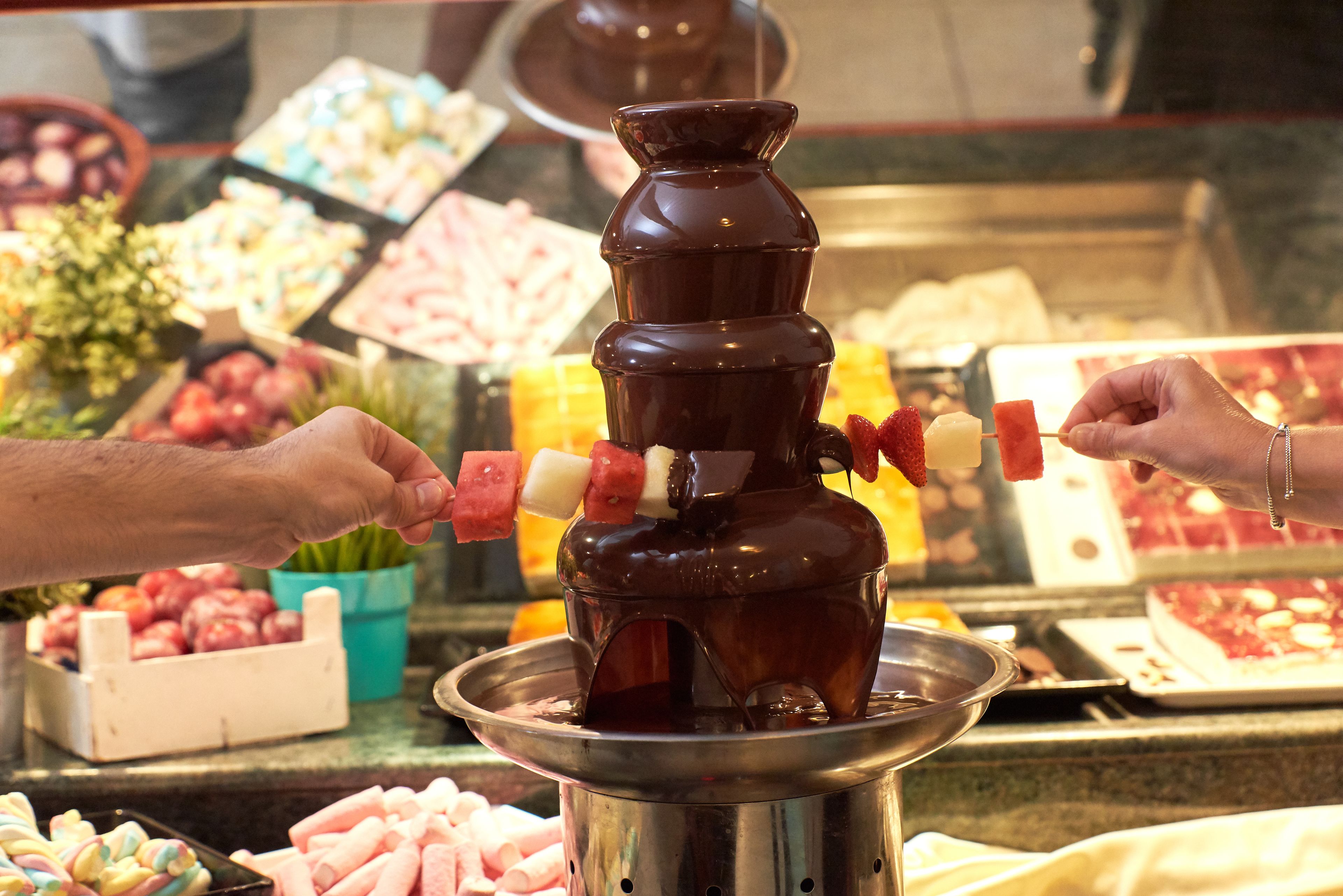Una fuente de chocolate con brochetas de fresas y malvaviscos.