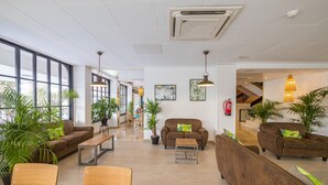 Eine großzügige Lobby mit großen Fenstern, verschiedenen Sitzbereichen und Zimmerpflanzen.