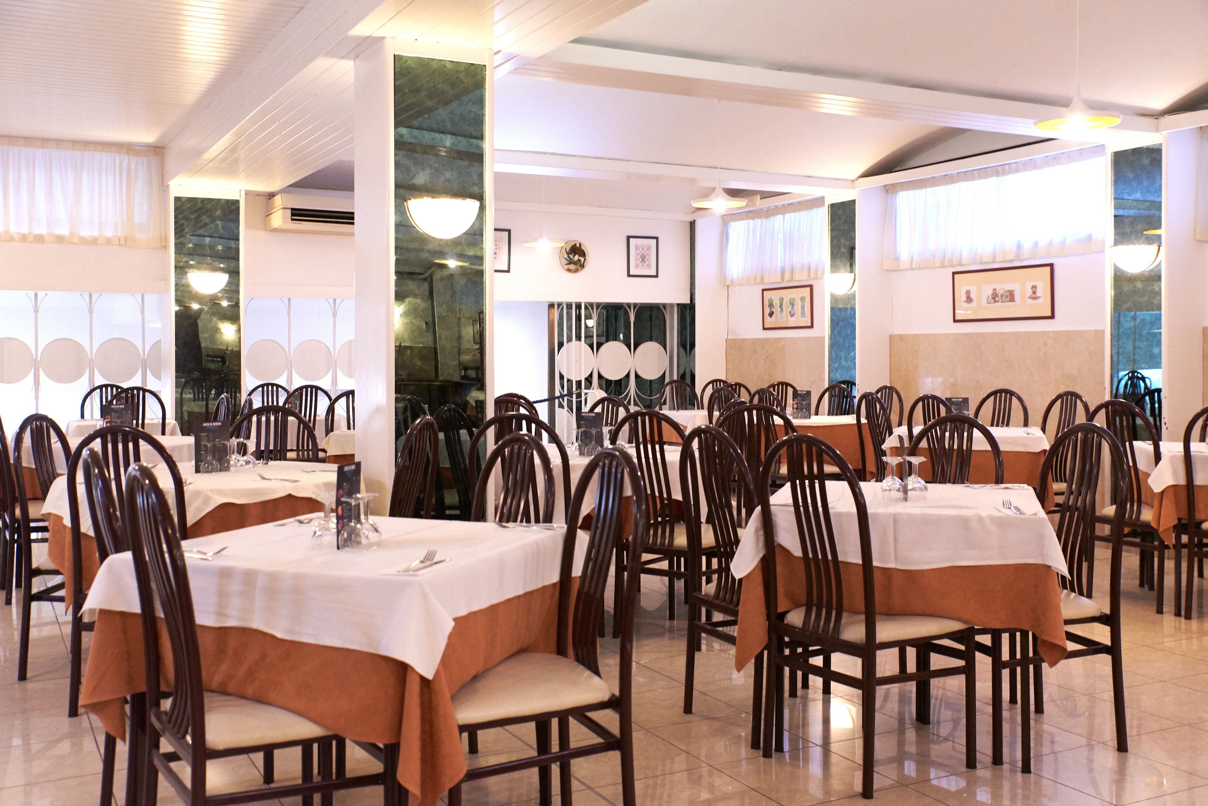 Un restaurante con varias mesas y sillas, manteles blancos y cuadros en las paredes.