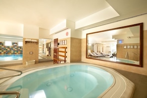 A hotel room with a large bathtub, a tiled wall, and a mirror reflecting the room. - Hotel Szárcsa (Szekesfehervar)