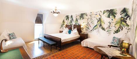 A hotel room with two beds, a bench, a small table, and a chair.