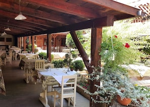 An outdoor dining area with wooden tables and chairs, covered by a wooden roof, surrounded by potted plants and flowers. - Hotel Szárcsa (Szekesfehervar)