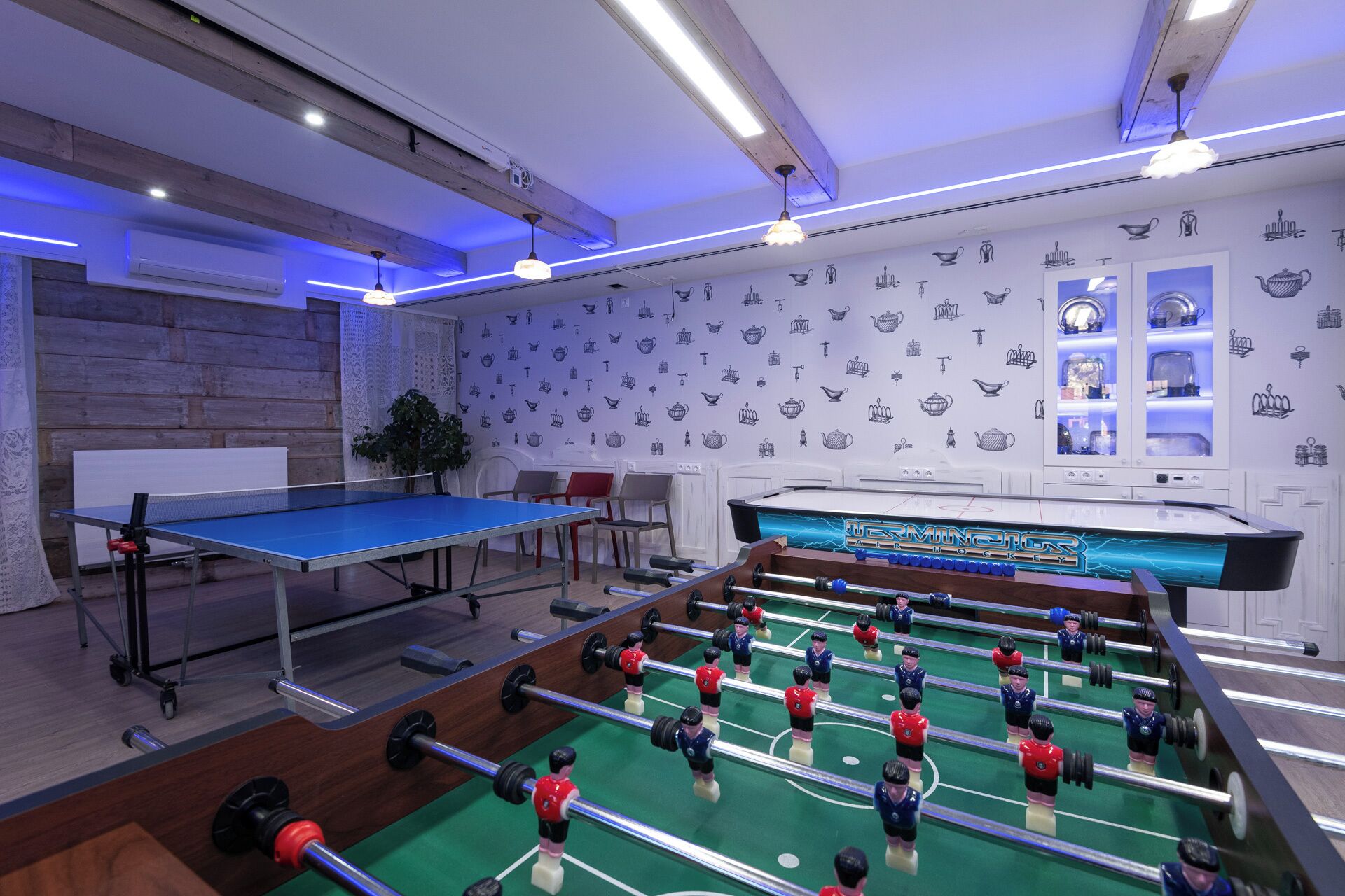 A room with a foosball table, ping pong table, and a wall with tea set illustrations.