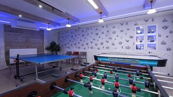 Et værelse med et bordtennisbord, et foosball-bord og en væg med illustrationer af tesæt.