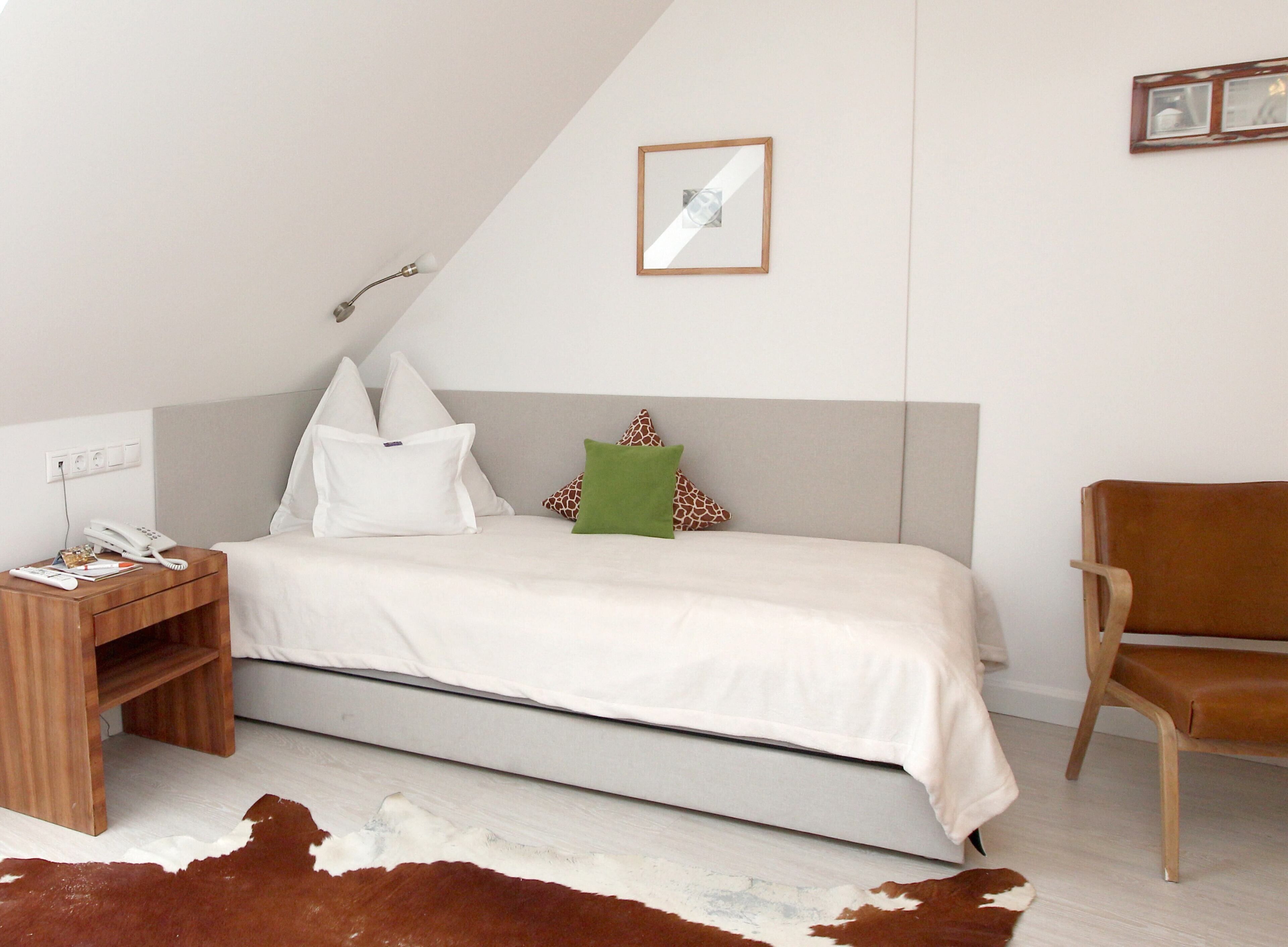 A bedroom with a bed, a nightstand with a phone, a chair, and a cowhide rug.