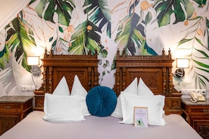 A hotel room with a large bed, two wooden nightstands, a telephone, and a wall with a tropical leaf pattern.