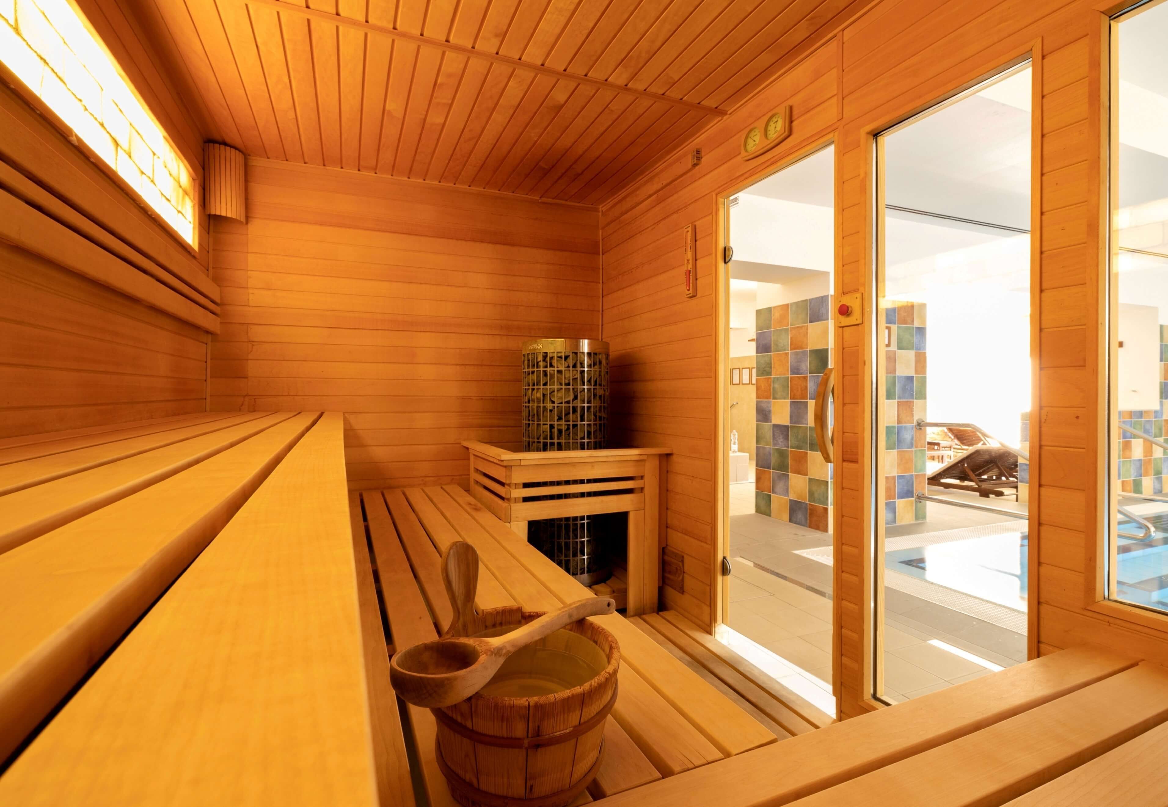 A wooden sauna room with benches, a wooden bucket, and a sauna heater.