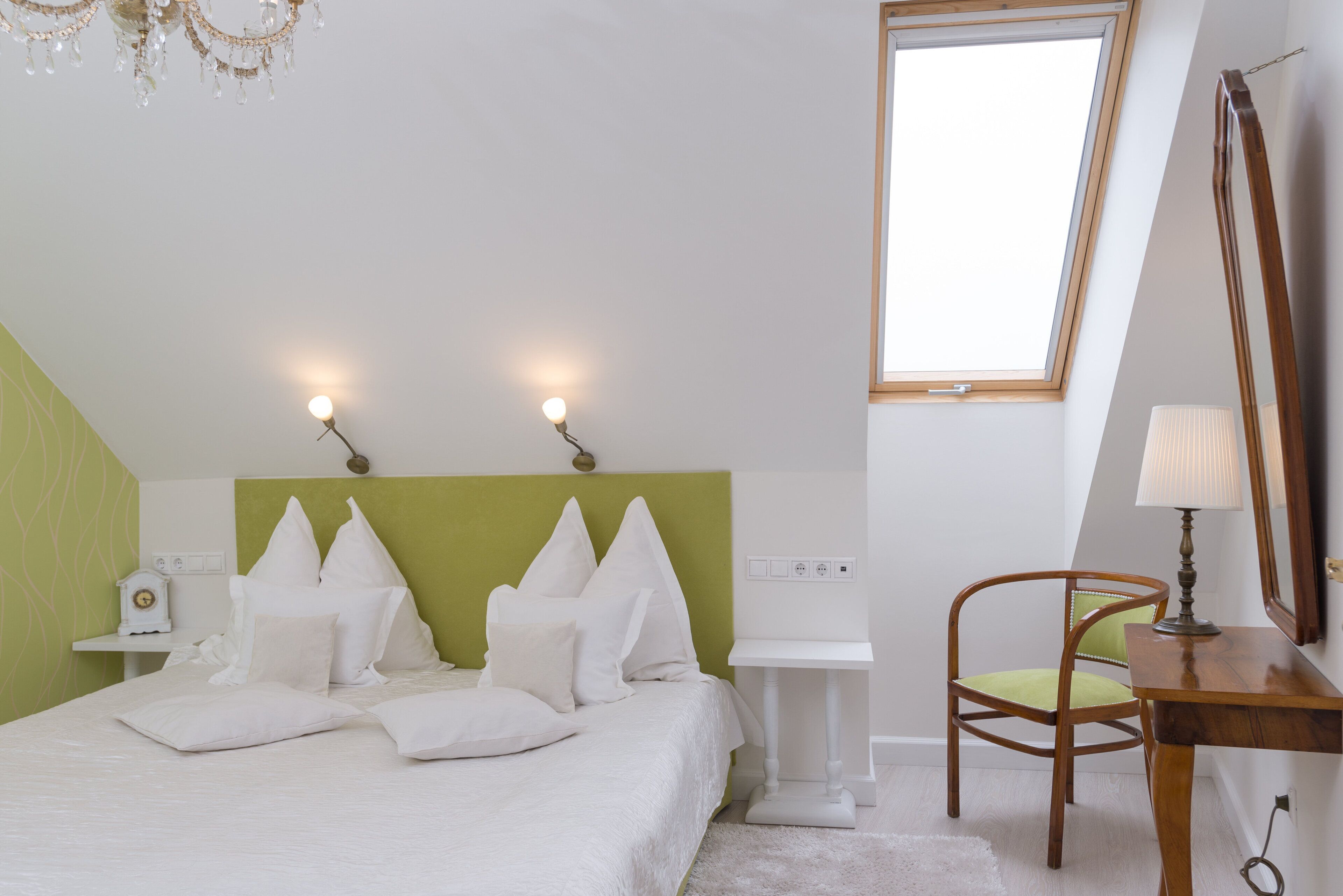 A bedroom with a bed, bedside table, chair, lamp, and a window.