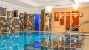 Una piscina interior con paredes de azulejos, una puerta azul y una zona de sauna de madera.