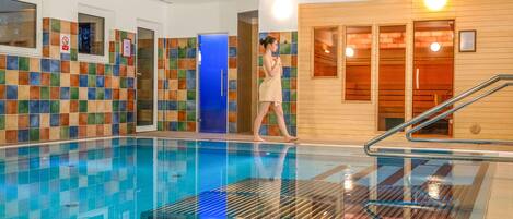 Una piscina interior con paredes de azulejos, una puerta azul y una zona de sauna de madera.