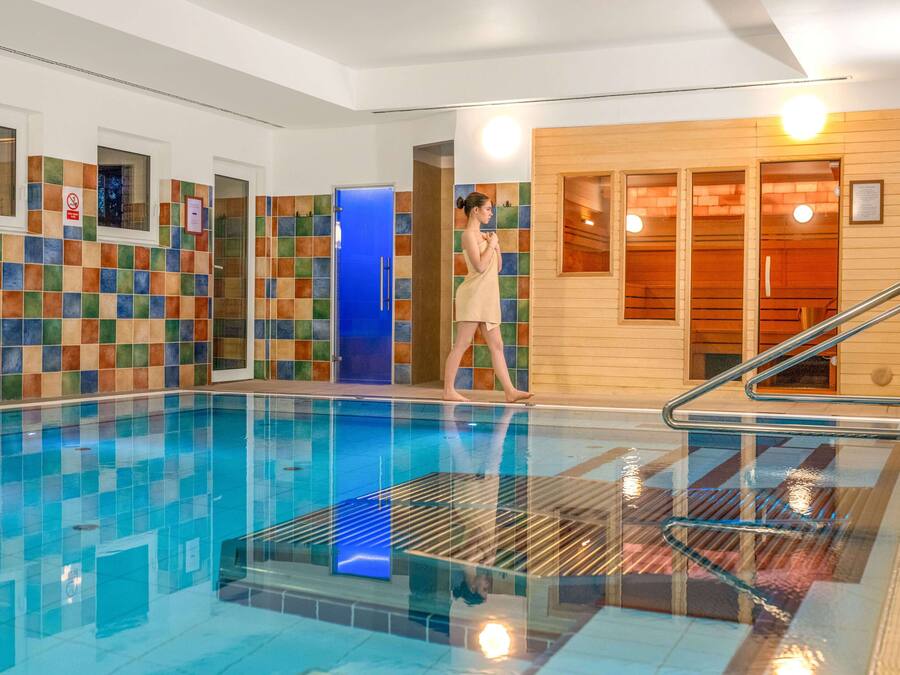 Una piscina interior con paredes de azulejos, una puerta azul y una zona de sauna de madera.