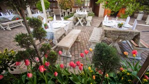 Un área de comedor al aire libre con mesas y bancos, rodeada de follaje y flores.
