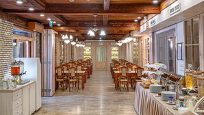 A long dining hall with wooden tables and chairs, a buffet area with food and drinks, and a brick wall on one side. - Hotel Szárcsa (Szekesfehervar)