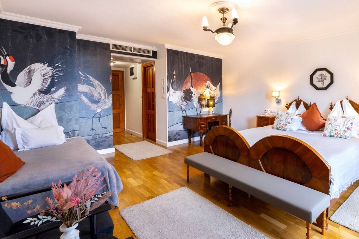 Ein Schlafzimmer mit Bett, Sitzbank, Nachttischen und einer Wand mit einem Gemälde.