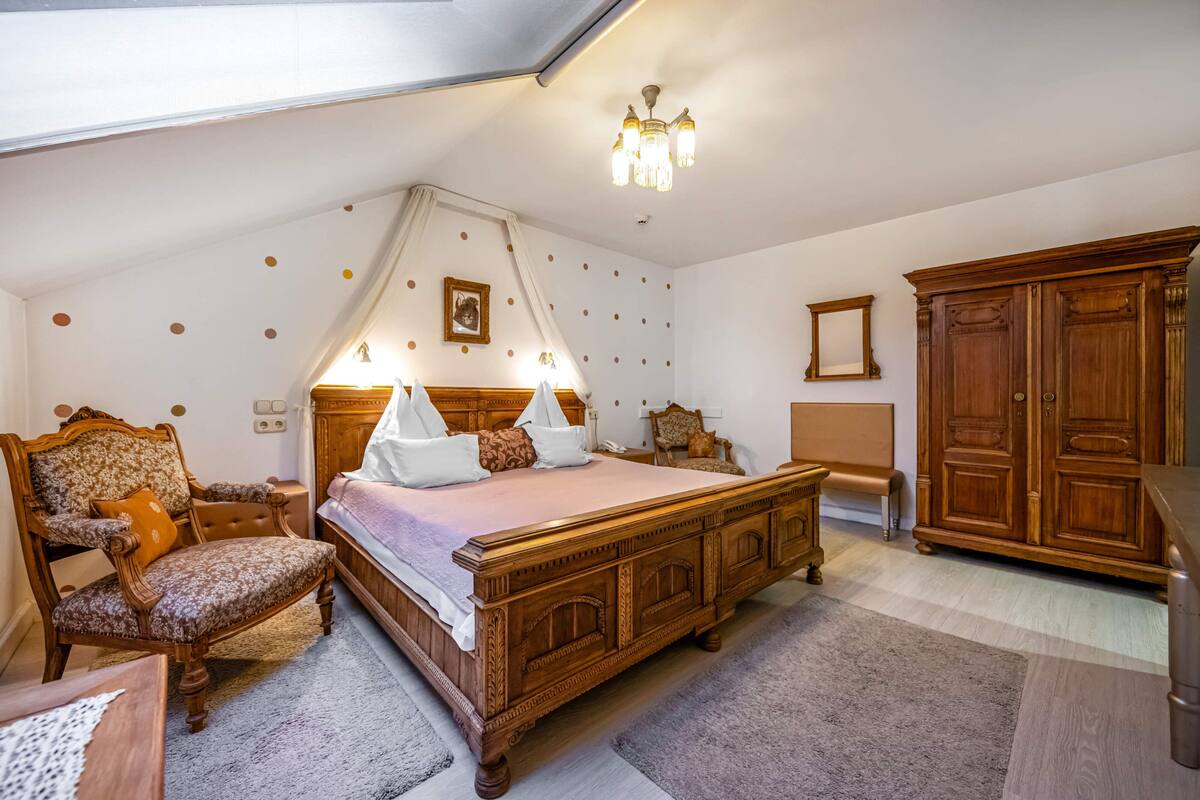 Ein Schlafzimmer mit einem großen Bett, einem Holzsessel, einem Kleiderschrank und einer Chandelier.