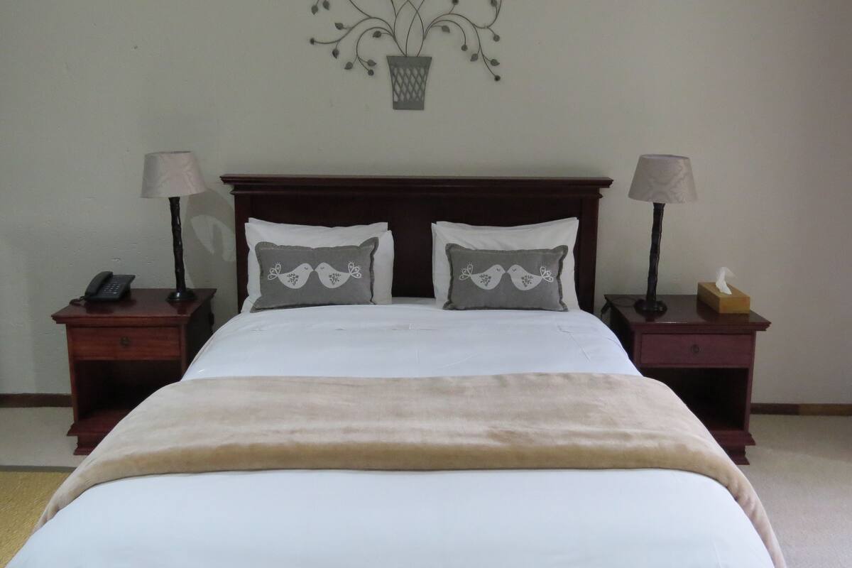 A neatly made bed with a beige blanket, two bedside tables with lamps, and decorative wall art above the bed.