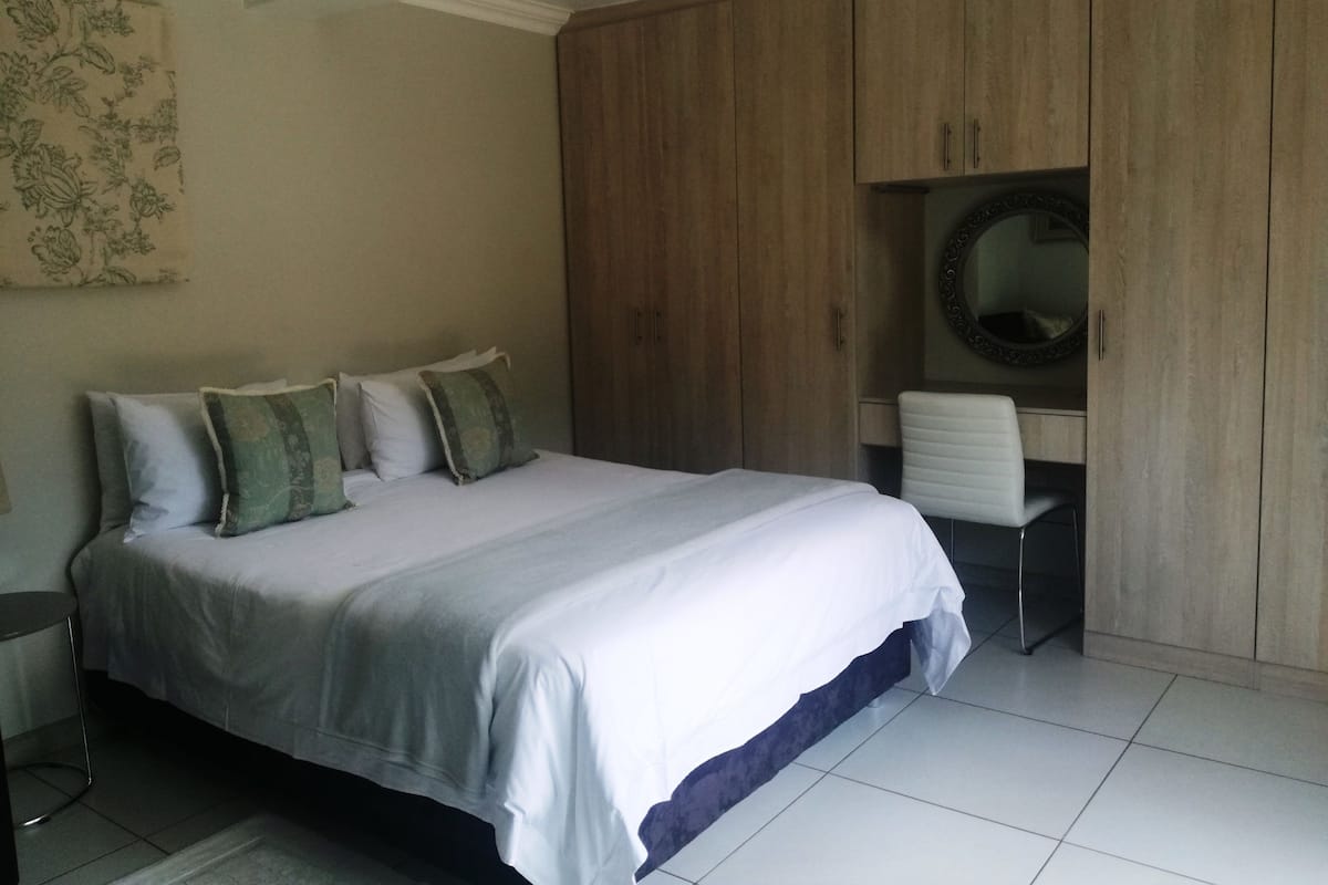 A bedroom with a bed, a chair, a wardrobe, and a mirror.
