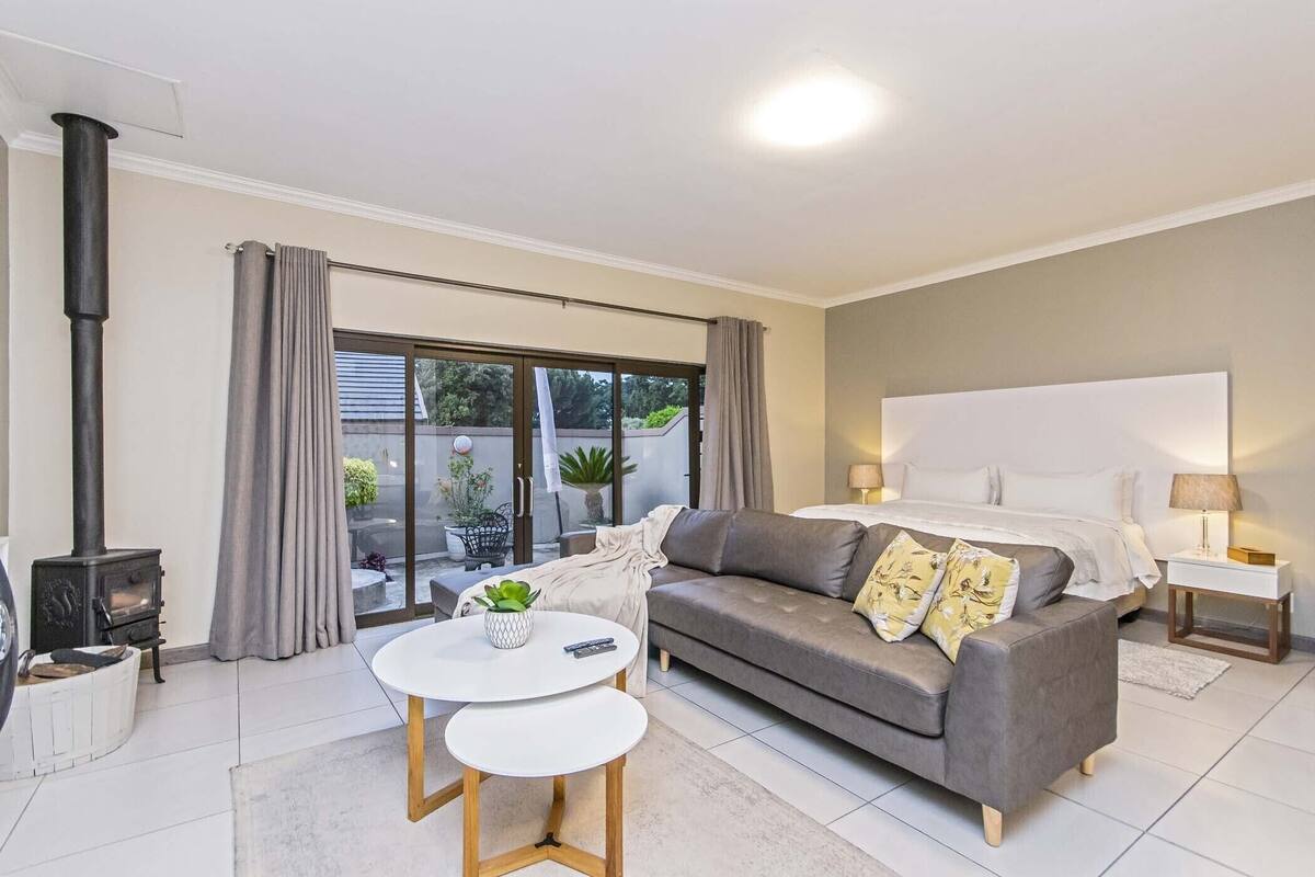A modern bedroom with a large bed, a grey sofa, a small white table, and a fireplace.