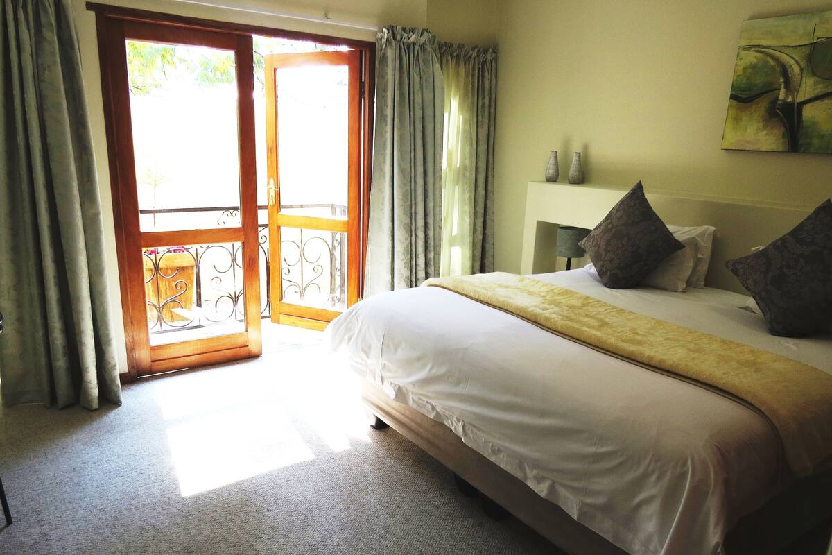 A bedroom with a bed, a nightstand, a painting, and a view through a glass door.