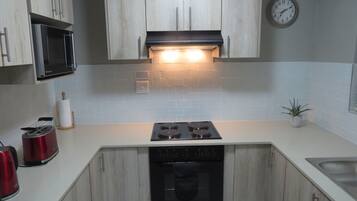 A kitchen with light wood cabinets, a black microwave, a stove, and a sink.