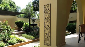 Une cour avec une fontaine, des plantes en pot et un panneau décoratif mural.