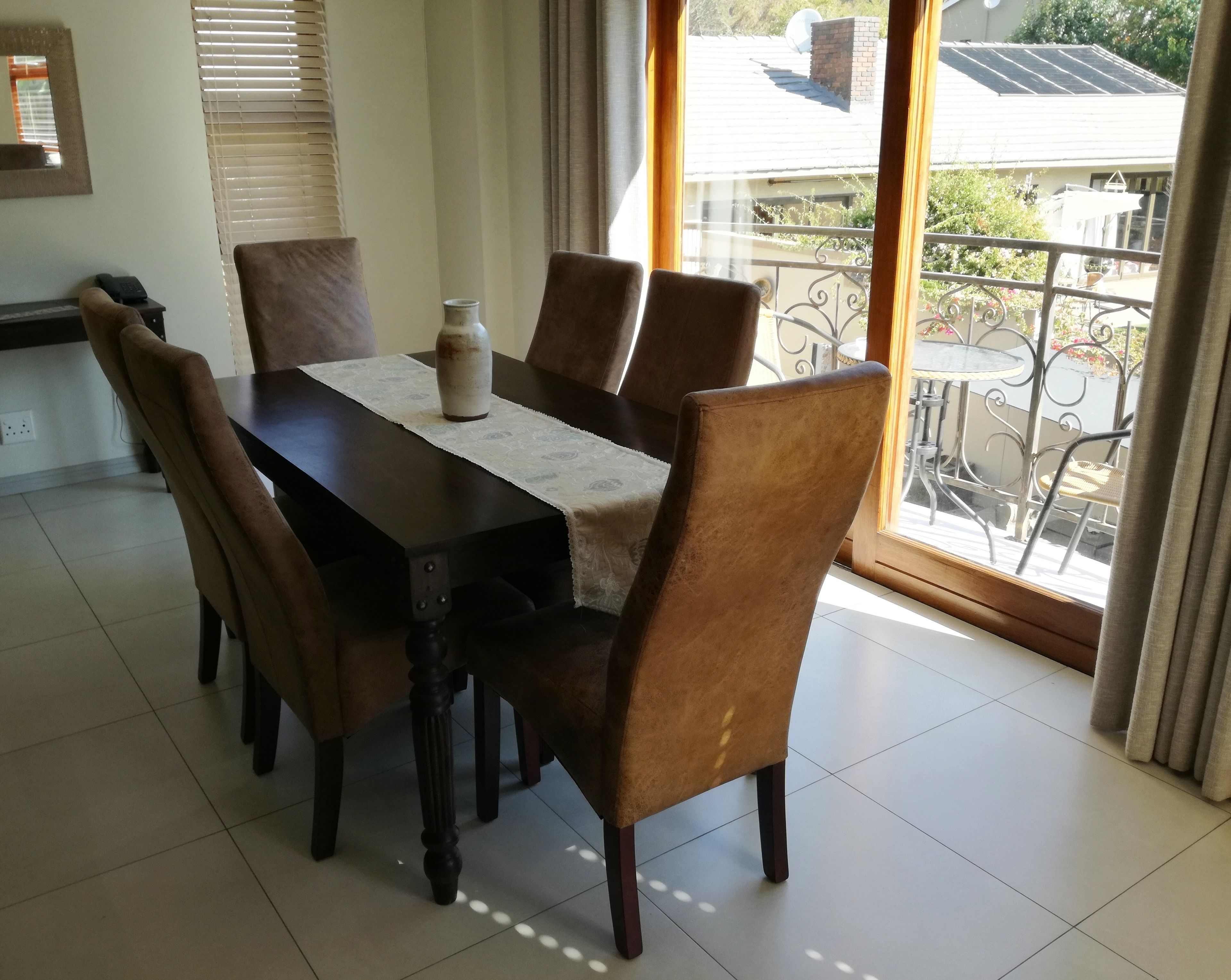 A dining area with a dark wooden table, six brown upholstered chairs, and a vase on the table.