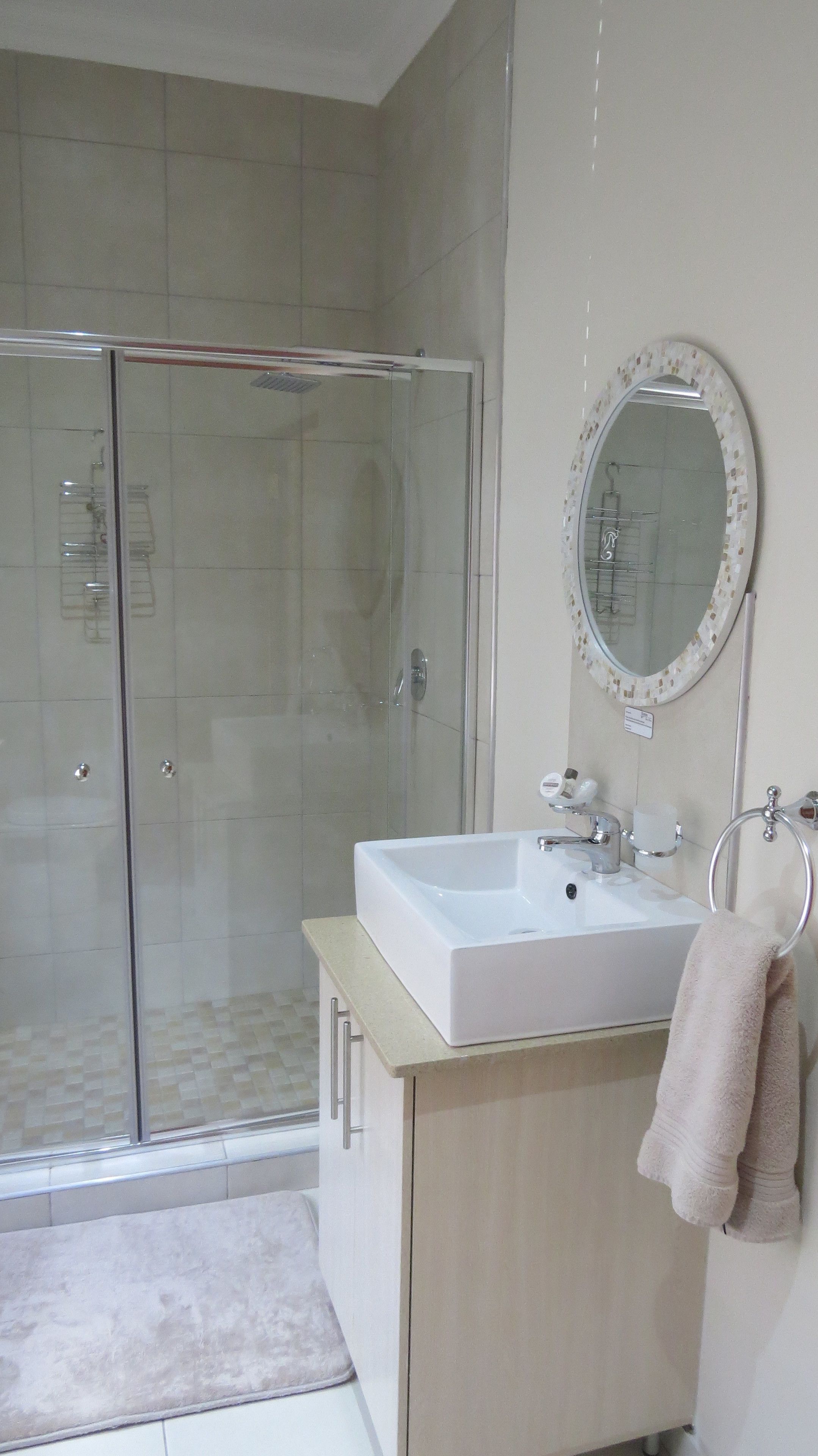 Un baño moderno con ducha envuelta en vidrio, un lavamanos blanco con espejo y un perchero para toallas.