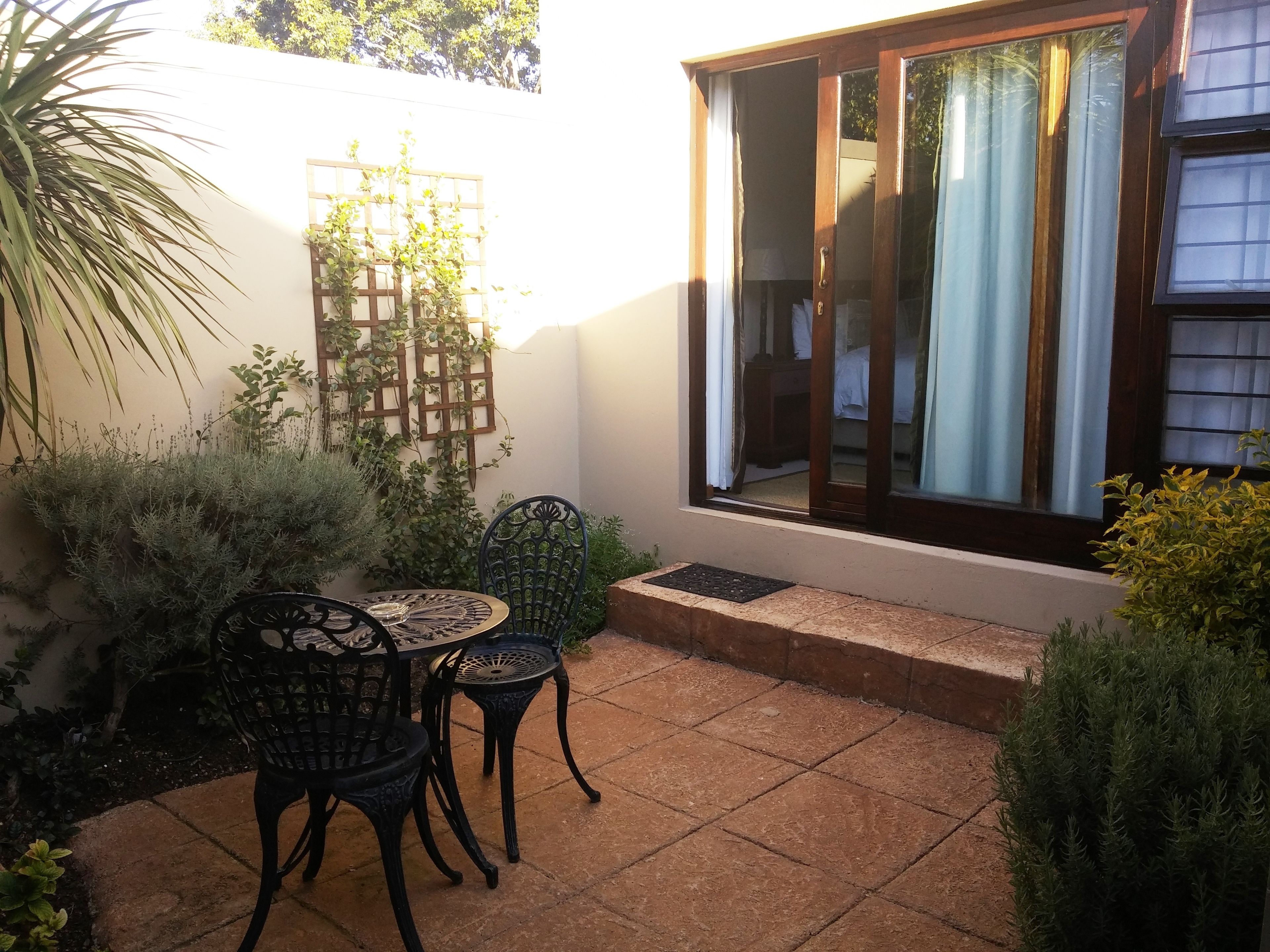 Un patio con mesa y sillas, un muro de celosía de madera y una ventana con cortinas.