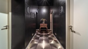 A hallway with a checkered floor, a wooden console table with a vase, and doors labeled 'C' and 'G'. - SleepWell Apartments Nowy Świat (Warsaw)