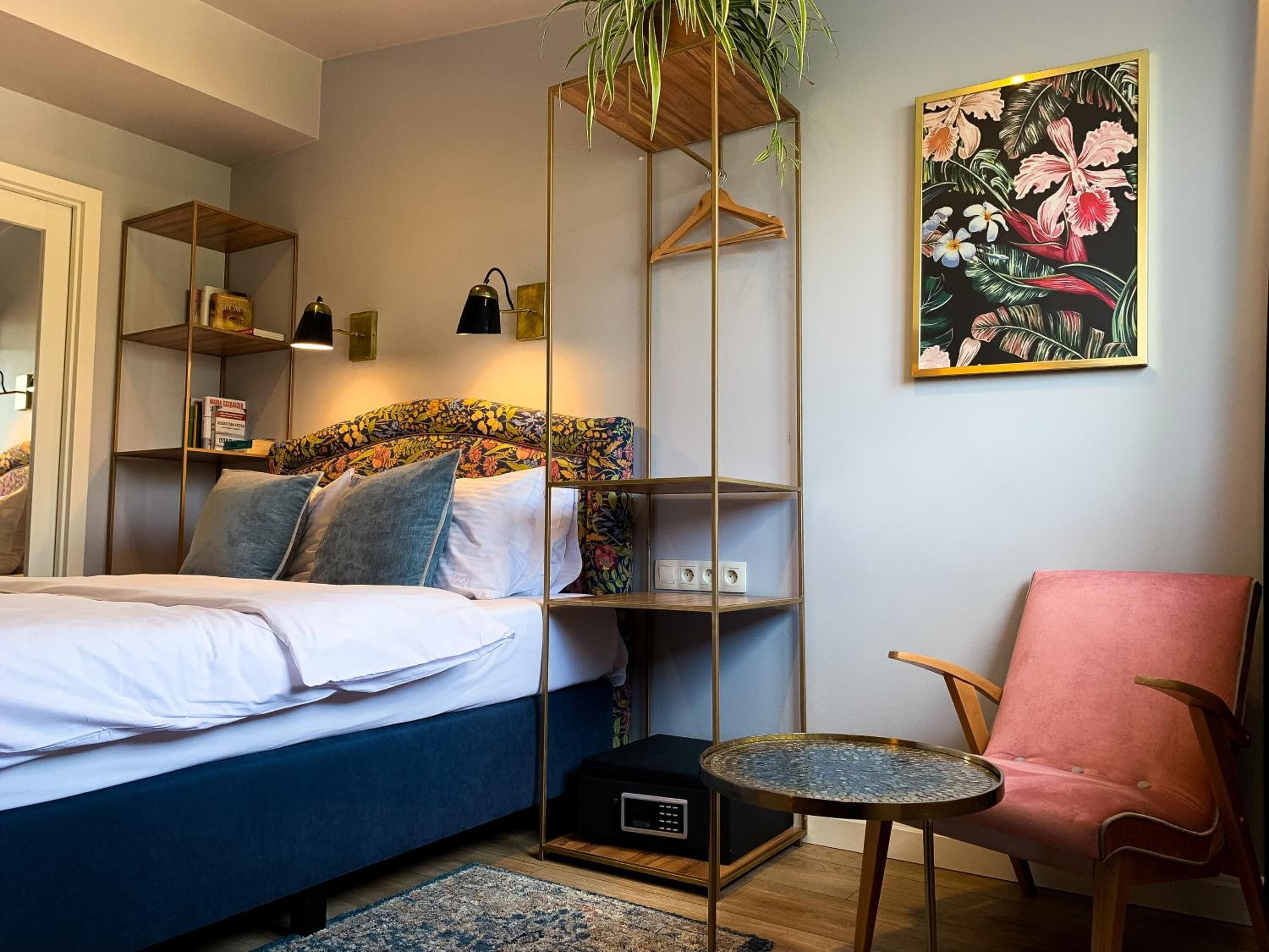 Una camera da letto con un letto, un comodino, una sedia, una libreria e una pianta pensile.