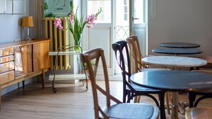 A dining area with wooden chairs and tables, a radiator, a lamp, and a poster on the wall. - SleepWell Apartments Nowy Świat (Warsaw)