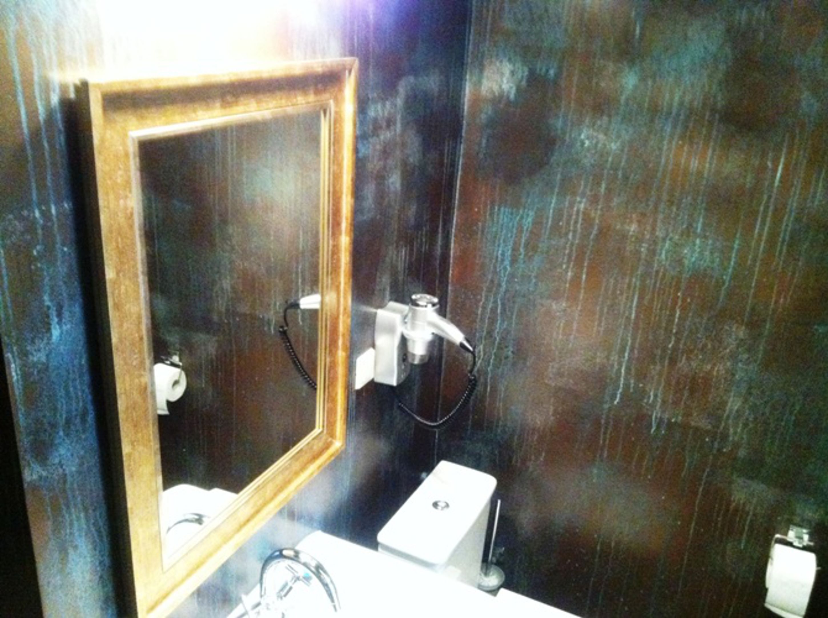 Un bagno con uno specchio con cornice in legno, un lavandino bianco e un portascopevoli.
