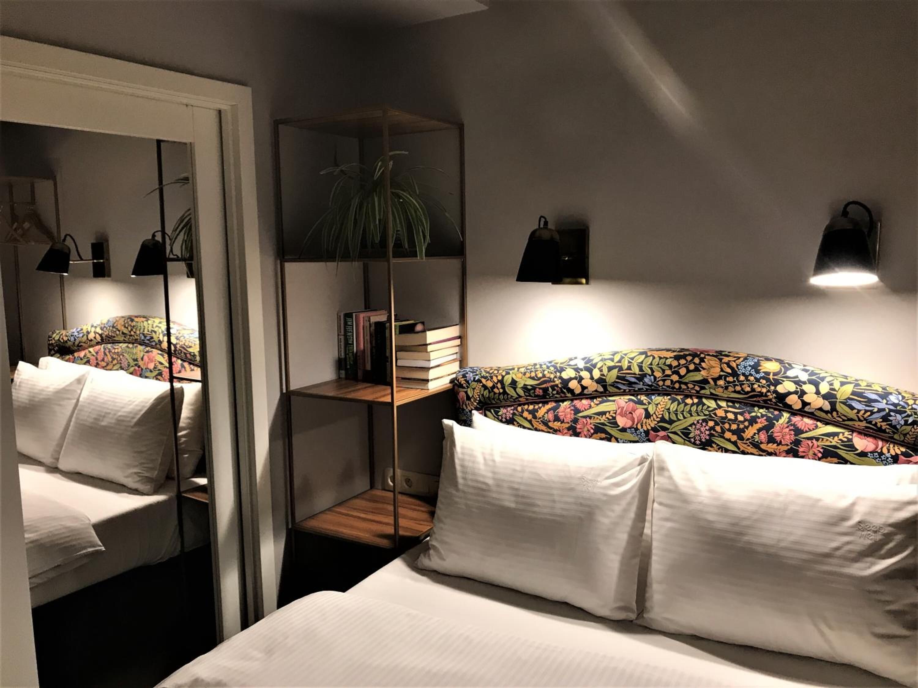 A bedroom with a mirrored wardrobe, a bedside table with a plant, and a bed with floral bedding.